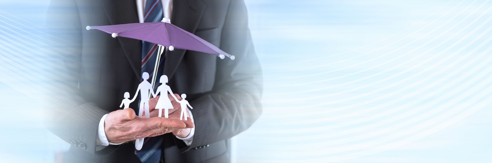 A businessman holding a paper cutout family protected under a miniature purple umbrella, against a soft abstract blue background